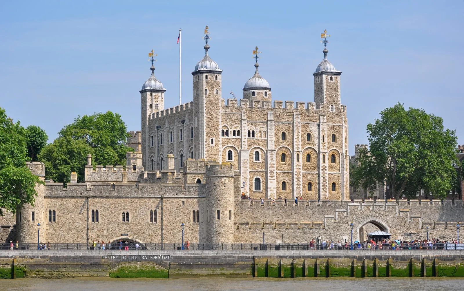 The stone ramparts and White Tower of the Tower of London viewed across the River Thames under a clear blue sky