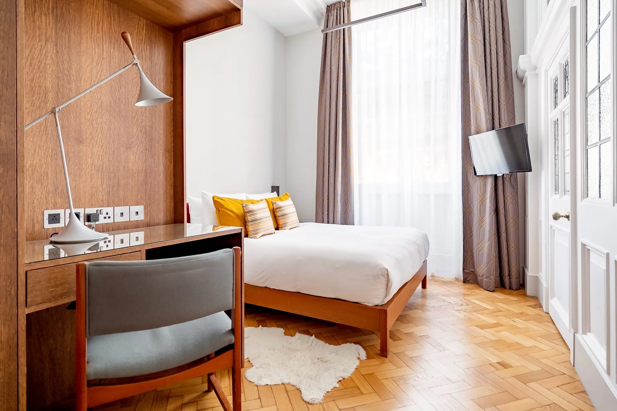 A room at Town Hall Hotel with mustard cushions, wood panelling and a sheepskin rug on parquet flooring