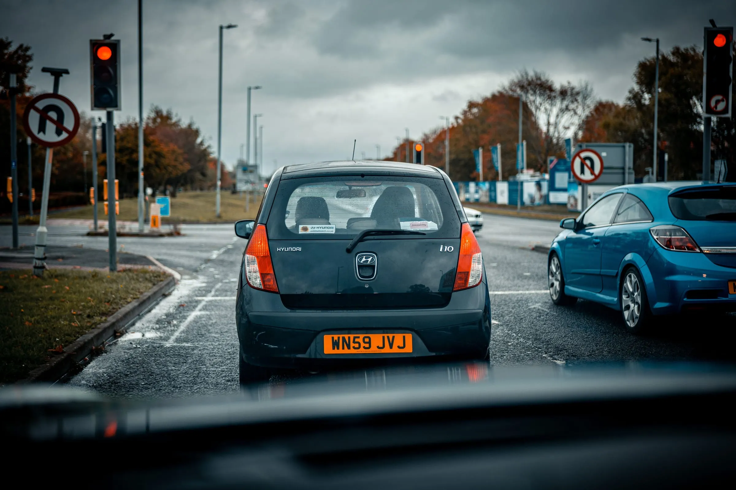 The view through a windscreen of a small car waiting at a red traffic light on a wet road