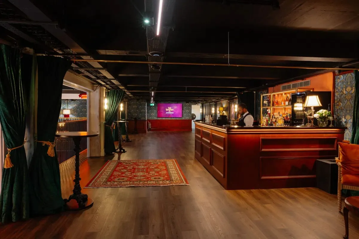 The bar at The Traitors Live Experience, panelled in dark wood with green velvet curtains and patterned wallpaper