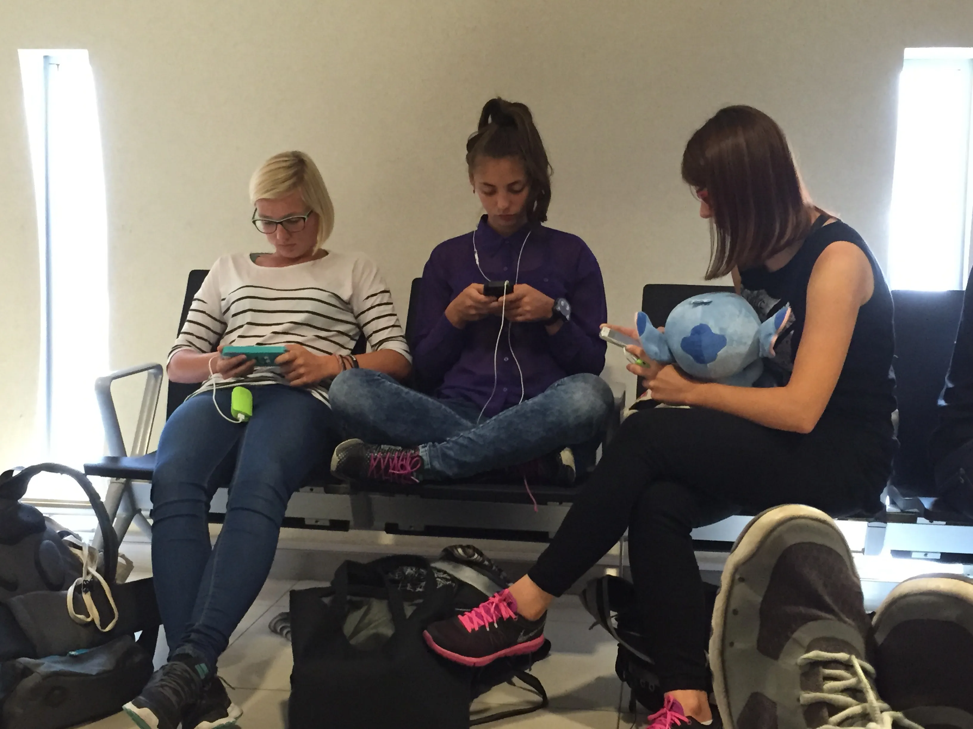 Three young travellers using smartphones while seated in a waiting area