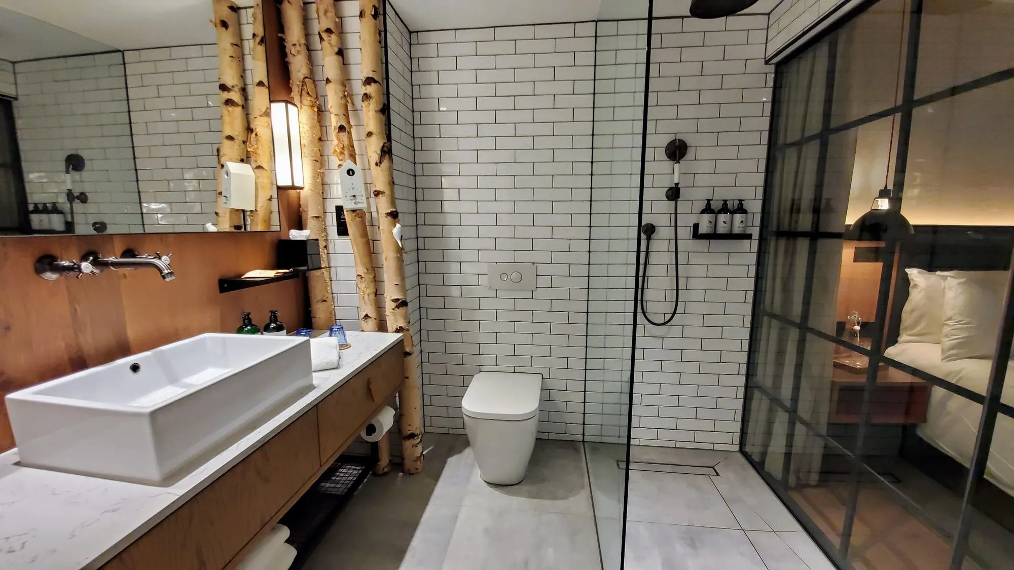 The bathroom at Treehouse Hotel London, with silver birch branches built into the tiled wall beside the walk-in shower