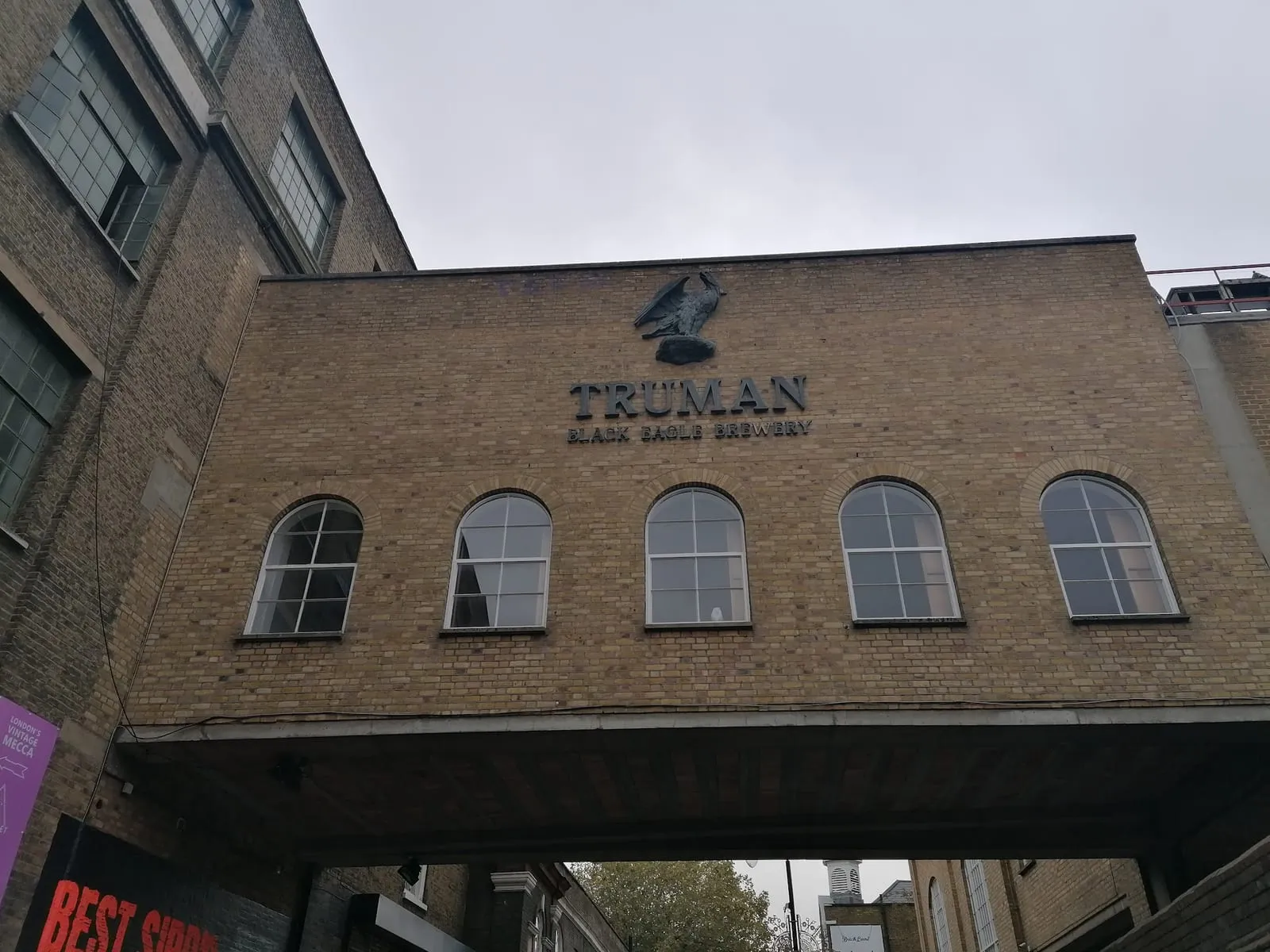 The Truman Black Eagle Brewery name and eagle on a brick bridge spanning Brick Lane under a grey sky