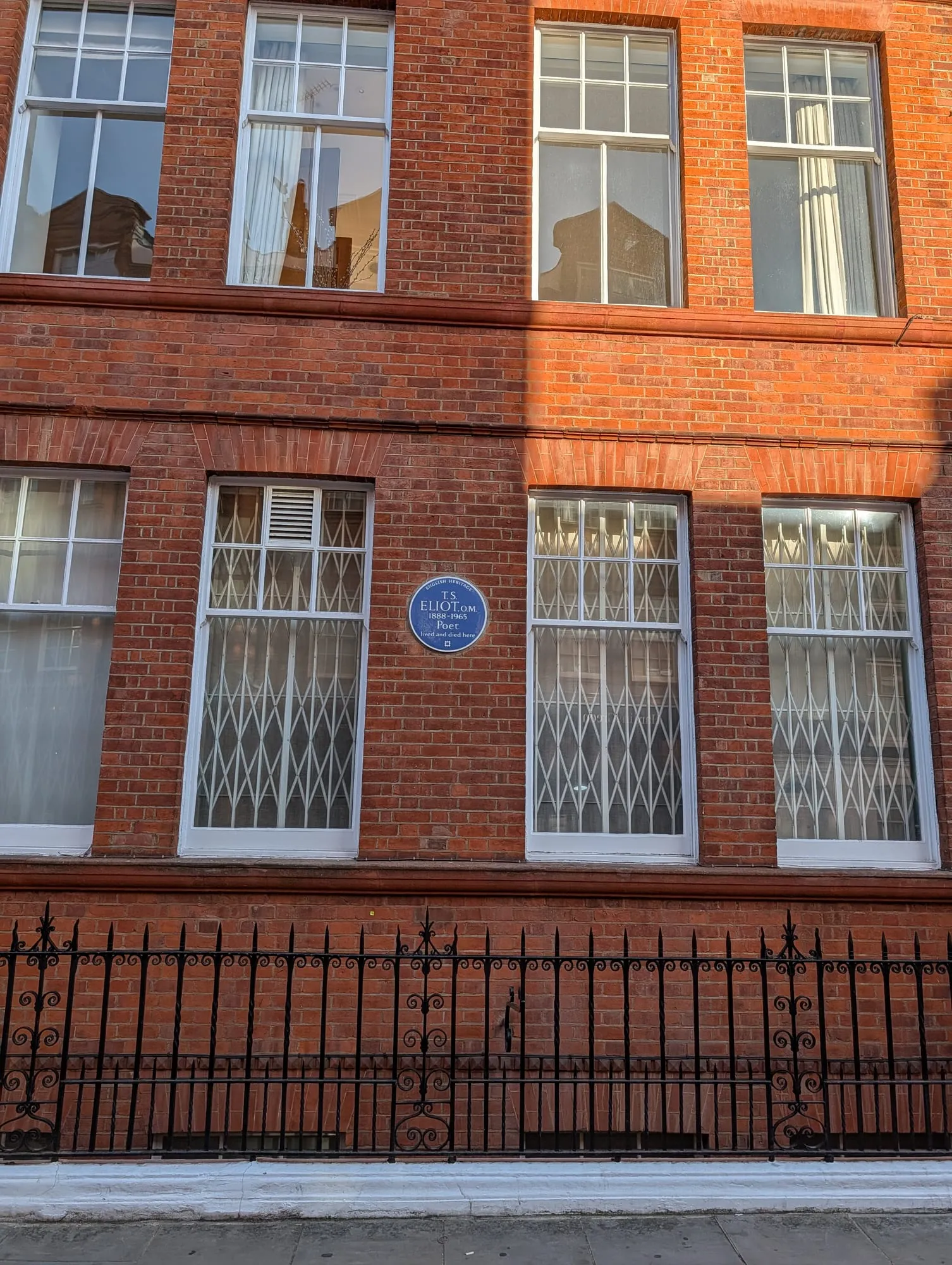 An English Heritage blue plaque to T.S. Eliot on the red brick front of a mansion block, between tall white sash windows
