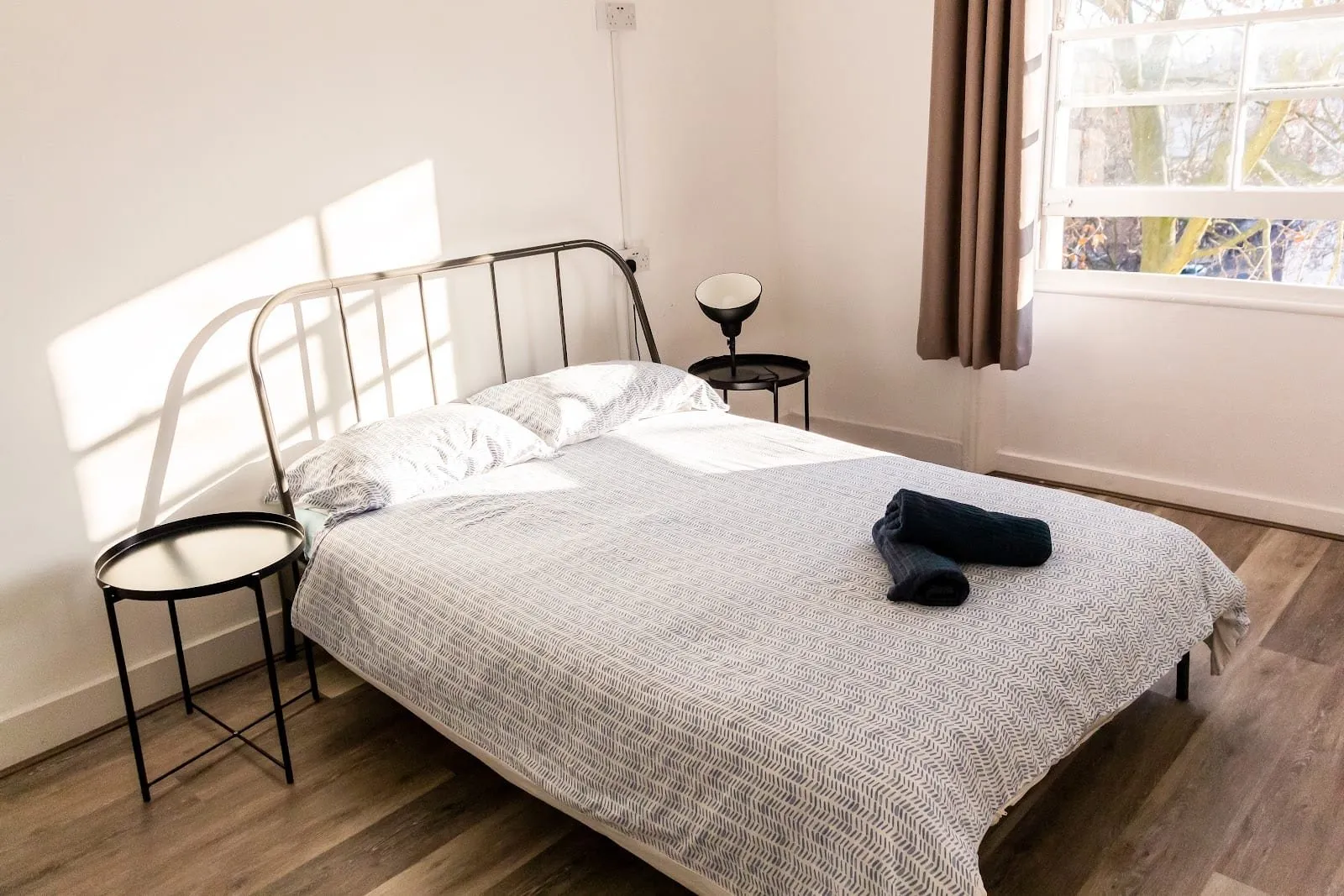The private double at Urbany Hostel London, with a metal-framed double bed, a herringbone-print duvet, black side tables and a large window onto trees