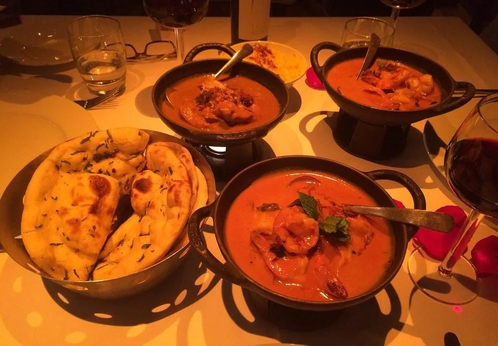 Brass karahis of prawn and chicken curry on the table at Veeraswamy, with a dish of garlic and coriander naan and a glass of red wine