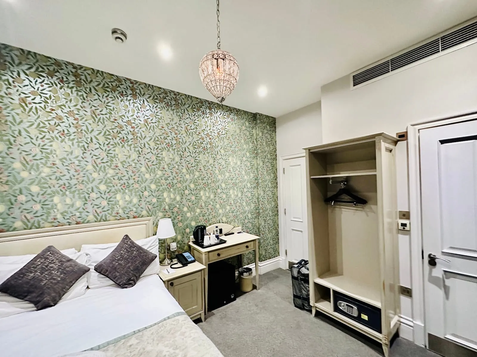 A double room at W12 Rooms with leaf-patterned wallpaper, a glass chandelier and a small desk with a kettle