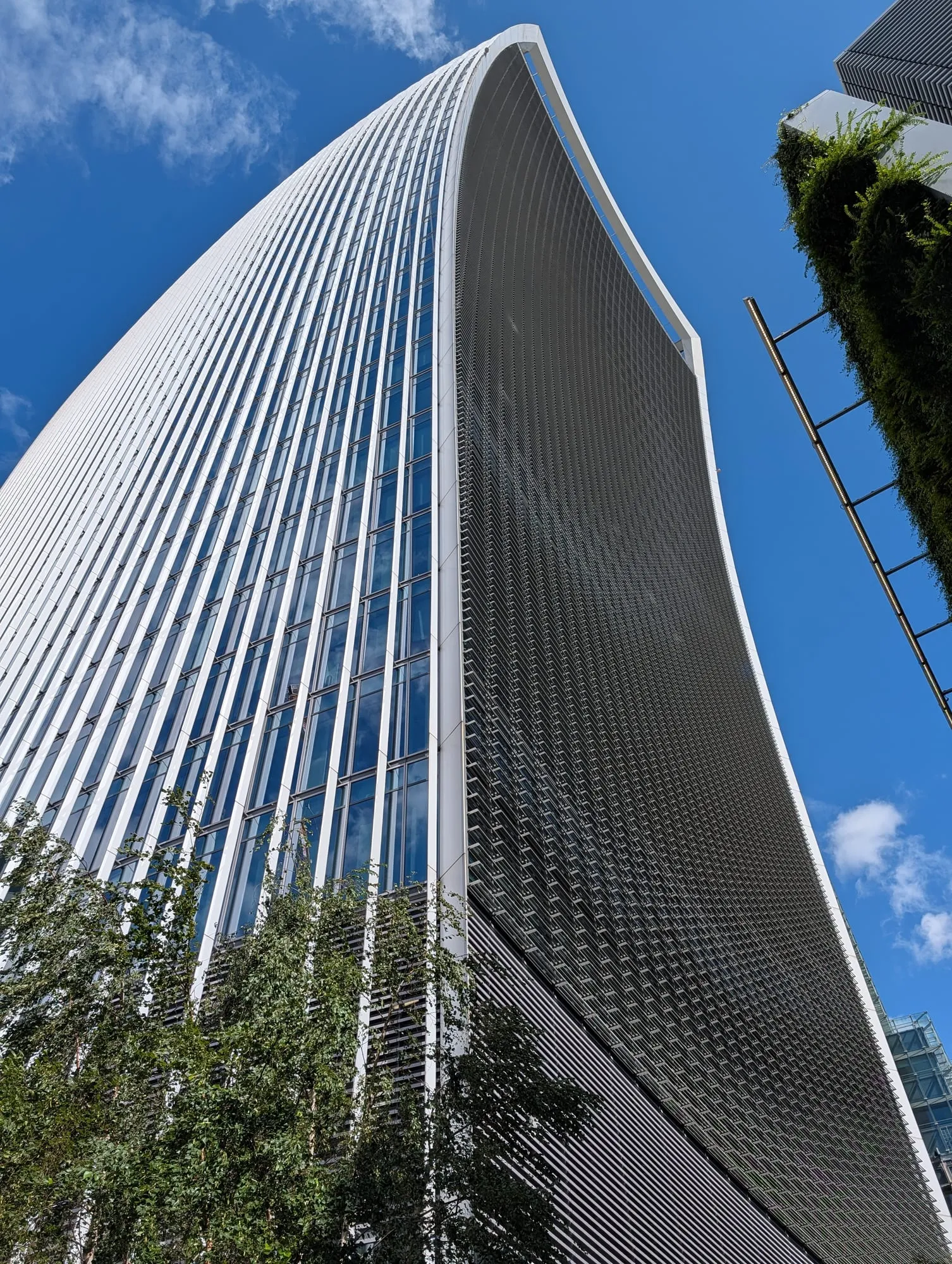 The curved glass flank of 20 Fenchurch Street, the Walkie-Talkie, seen from the pavement directly below and flaring outwards towards the top