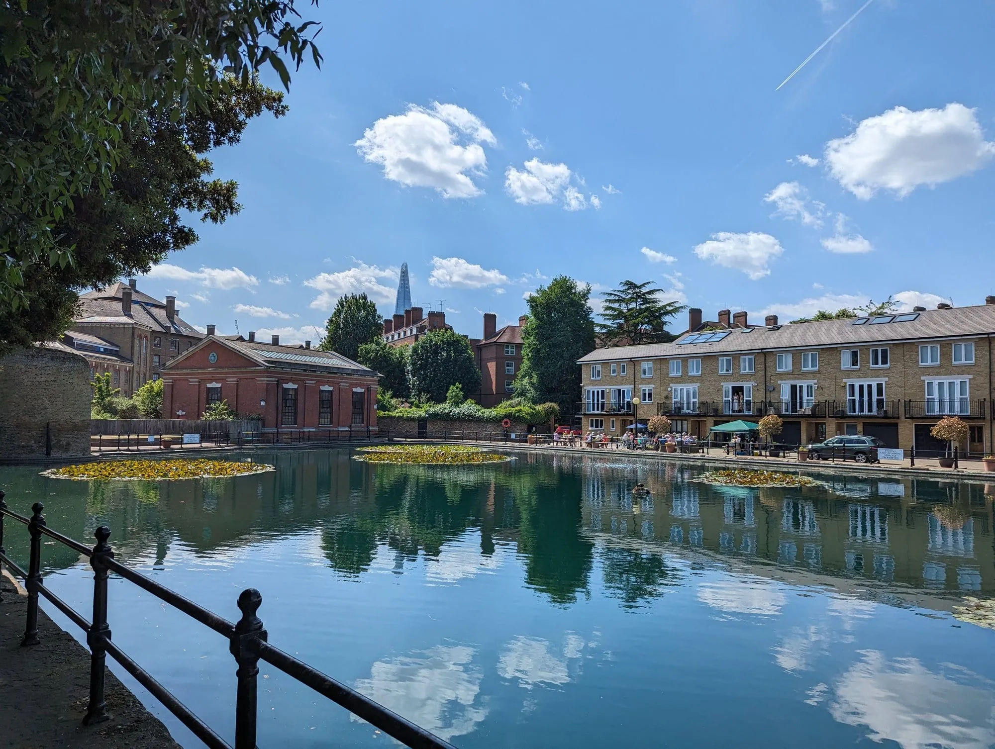 A still Wapping dock lined with converted Georgian and Victorian warehouse flats, reflecting the buildings and sky, with the Shard visible on the skyline in the distance