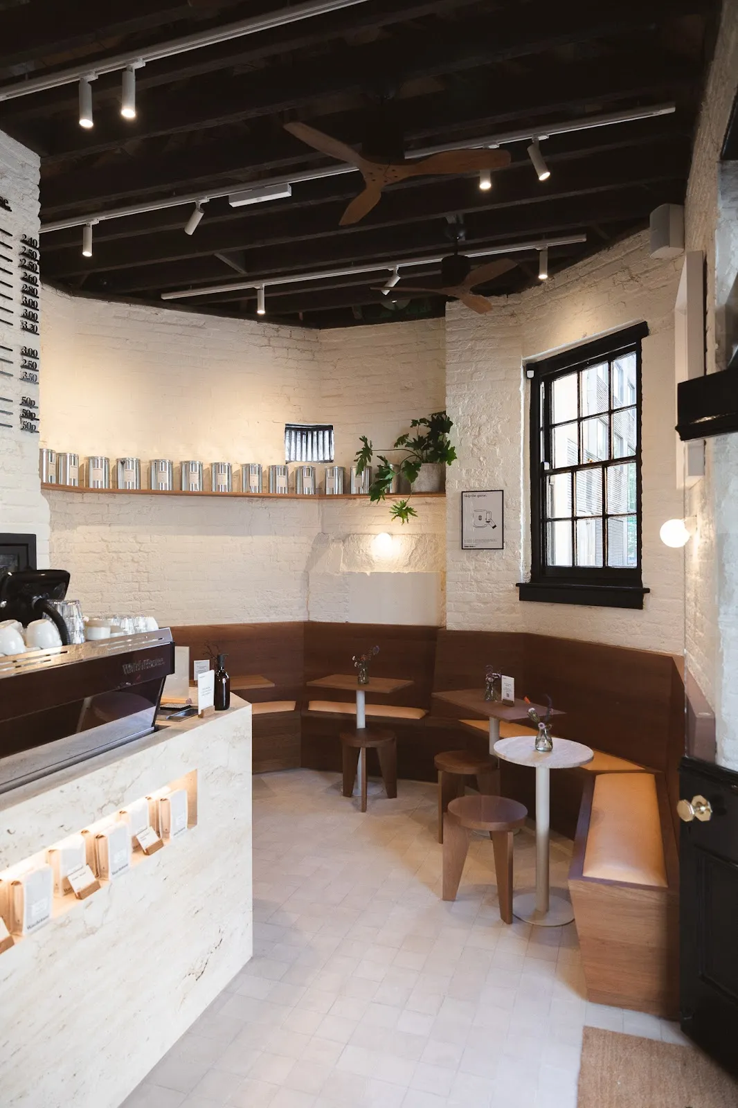The curved interior of WatchHouse in Bermondsey, with a coffee counter, small round tables and a beamed ceiling