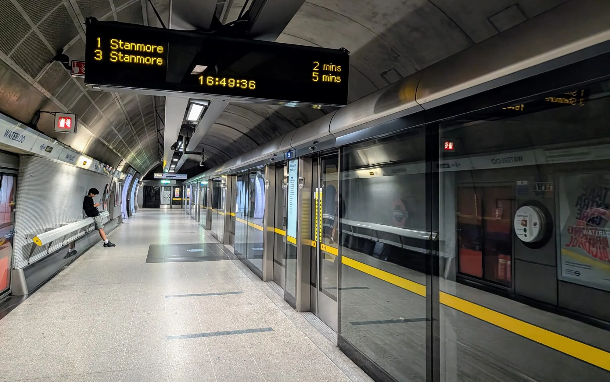 A dot matrix indicator above a Jubilee line platform at Waterloo reading 1 Stanmore 2 mins and 3 Stanmore 5 mins, above a train behind platform edge doors