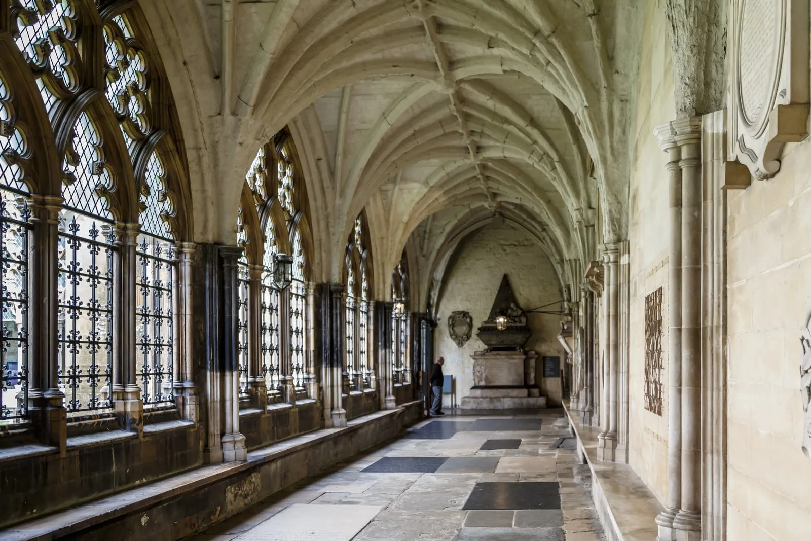 Medieval stone vaulted cloister walkway with traceried windows opening onto the lawn