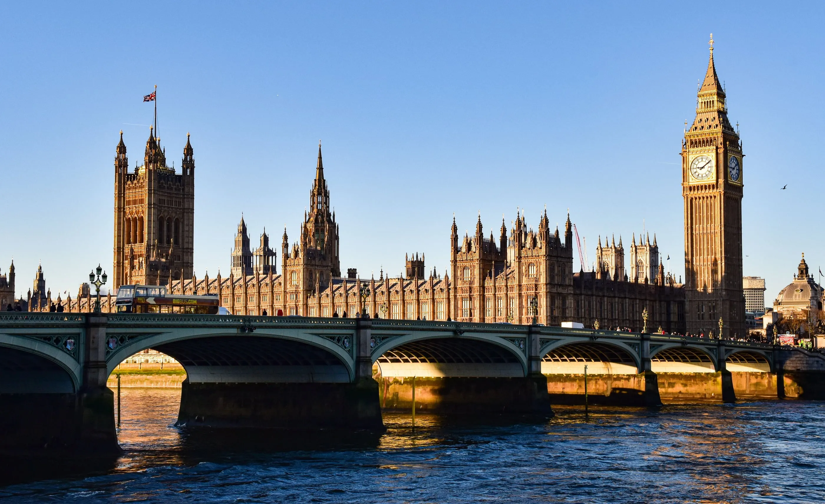 The Houses of Parliament, Elizabeth Tower and Westminster Bridge lit by low golden sunlight from across the Thames