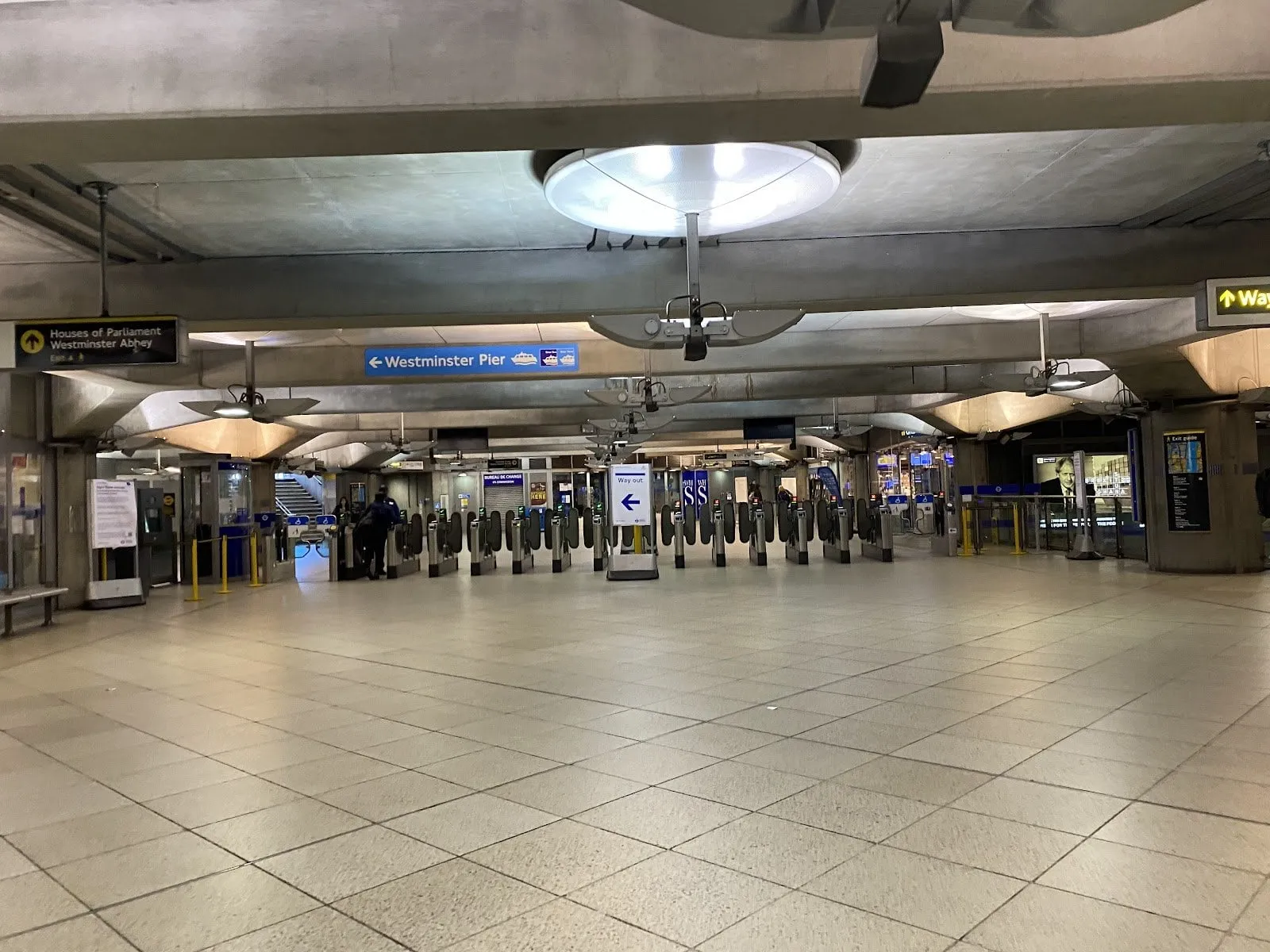 The ticket barriers in Westminster station's ticket hall under a bare concrete ceiling, signs pointing to the Houses of Parliament, Westminster Abbey and Westminster Pier