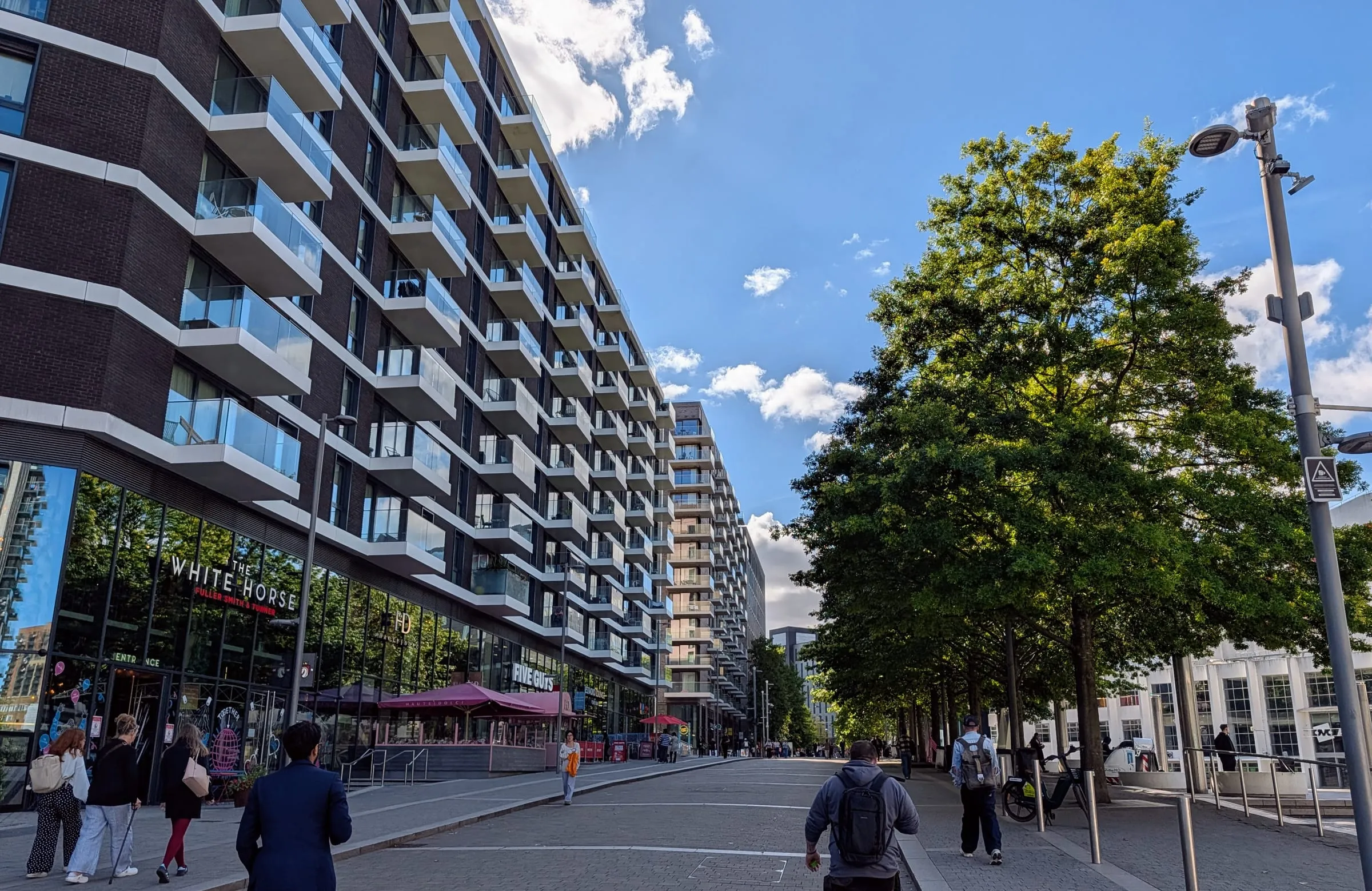 The White Horse pub on the ground floor of a tall apartment block on Wembley Park Boulevard, with outdoor tables and people walking past