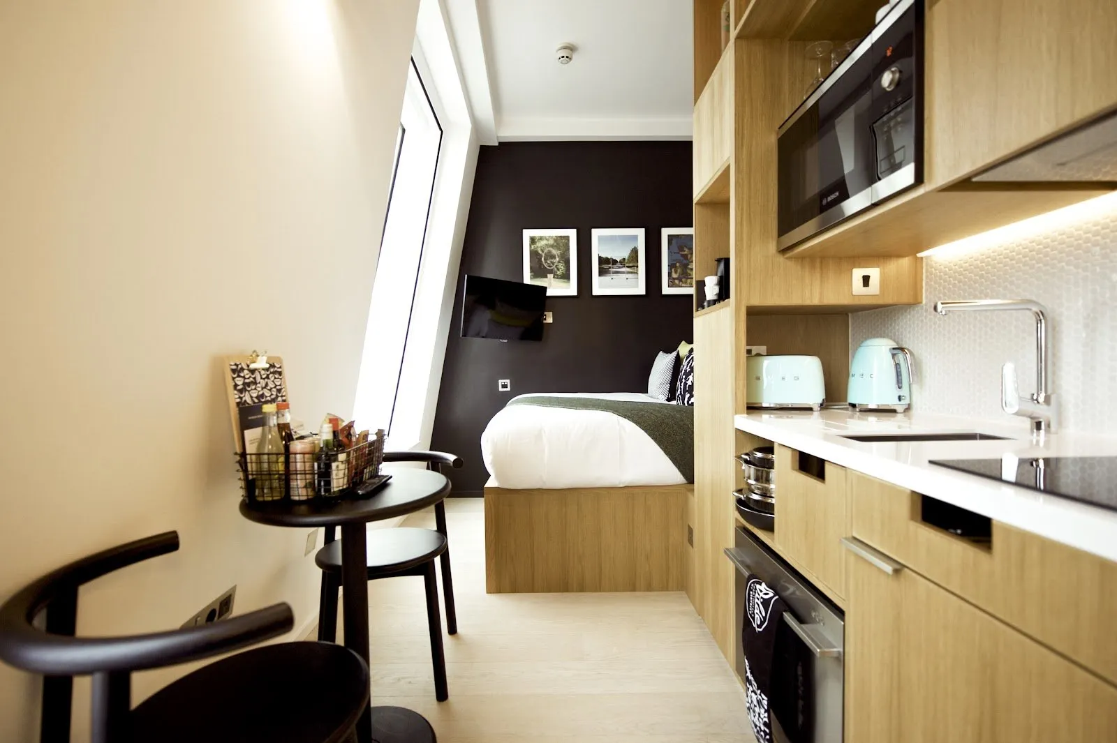A studio apartment at Wilde Covent Garden with a bed against a black accent wall and a full kitchen with a Smeg toaster and kettle beside it