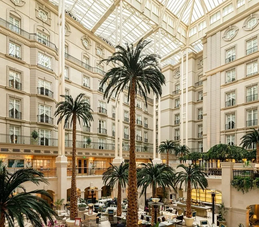 The eight-storey glass-roofed atrium of the Landmark London, with full-grown palm trees rising above the tables