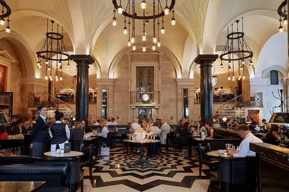The Wolseley's vaulted dining room, black and white floor, pillars and low-hung lamps, full of diners
