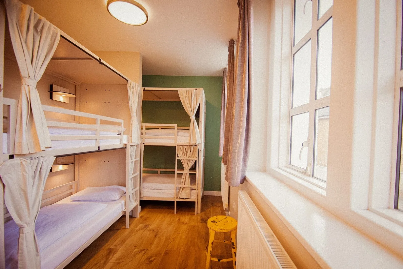 A dorm room at Wombat's City Hostel, with cream-curtained bunk beds against a green accent wall