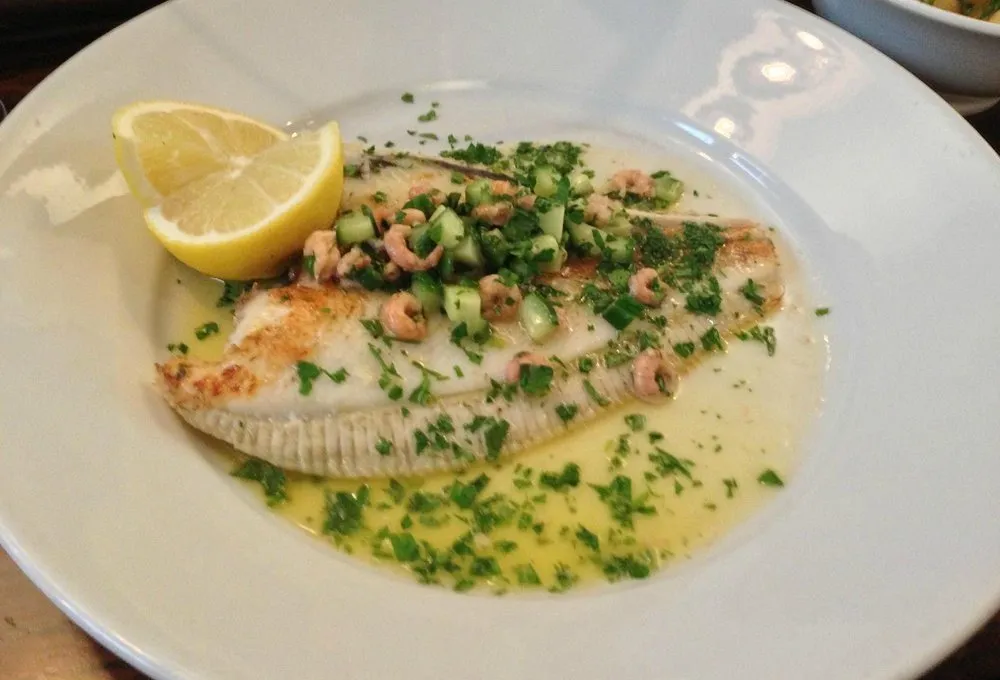 A whole plaice on the bone in a butter and parsley sauce, scattered with brown shrimp and diced cucumber, with a lemon half
