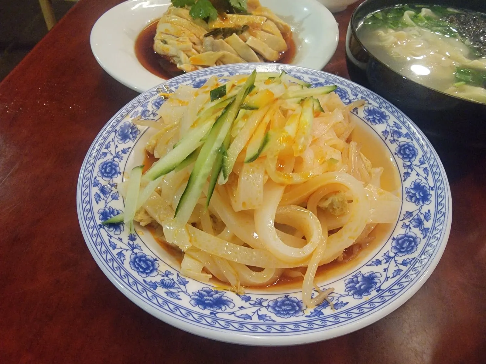 A bowl of cold liangpi noodles topped with julienned cucumber, in a blue and white patterned dish