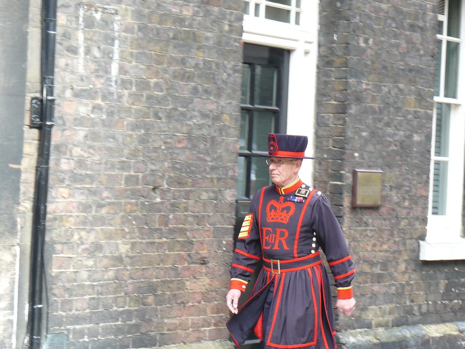 A Yeoman Warder in dark blue and red uniform addressing a group of visitors in the outer ward of the Tower of London