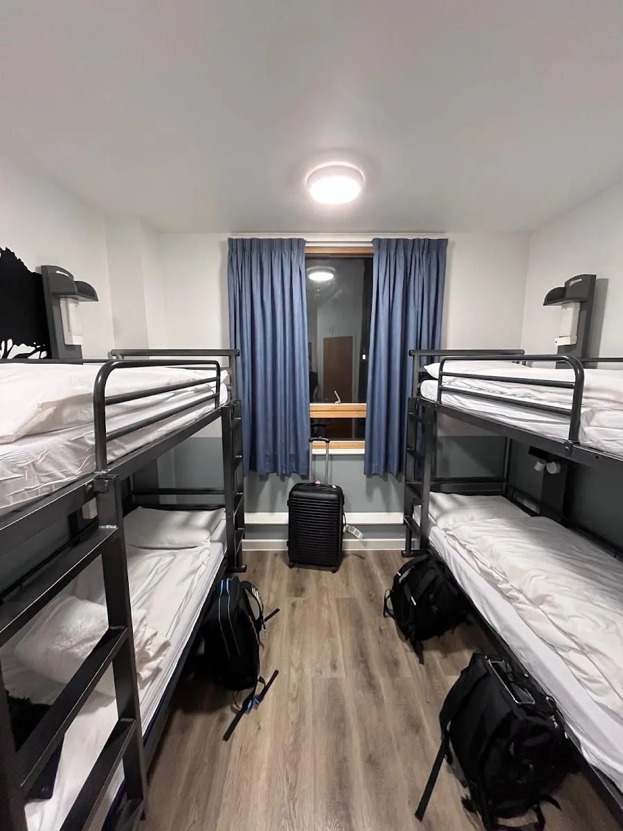 A shared room at YHA London Central, with metal bunk beds and blue curtains at the window