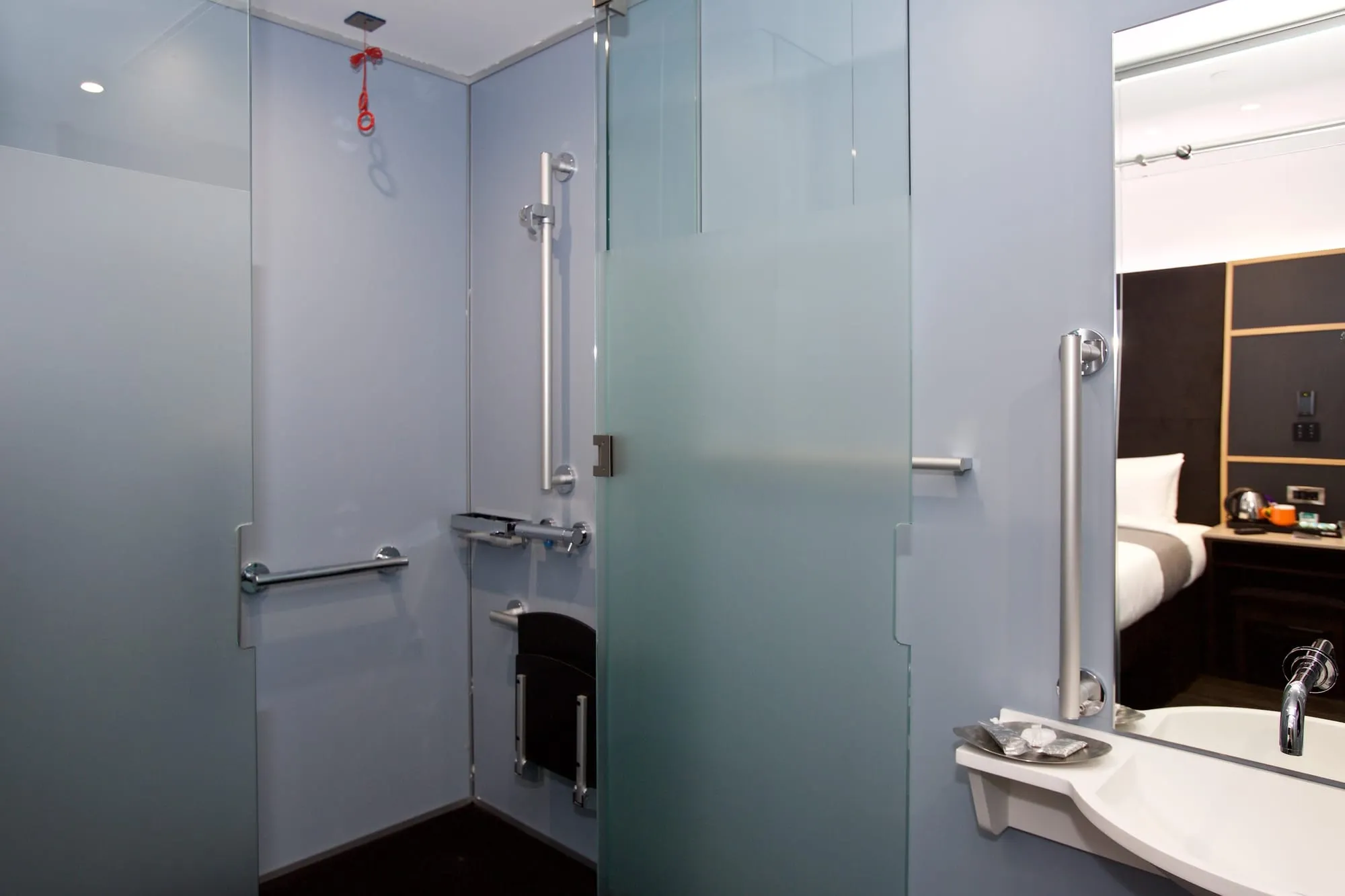 The ensuite bathroom of a Z Hotel Covent Garden room, with frosted-glass cubicle doors and chrome grab rails