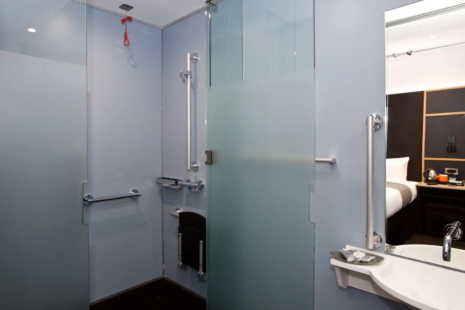 An ensuite bathroom at the Z Hotel Covent Garden, with a frosted-glass shower screen and wall-mounted grab rails