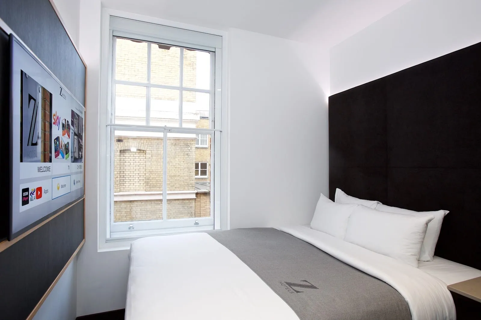A compact double room at the Z Hotel Covent Garden, with a dark upholstered headboard and a wall-mounted television showing the in-room welcome screen