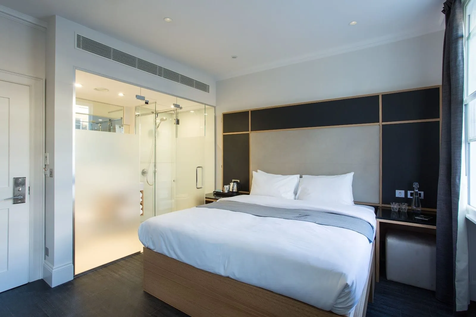The same Z Hotel Gloucester Place room from the other side: the bathroom is a glass box between the entrance door and the bed, frosted to about head height on the left, with the shower visible through clear glass