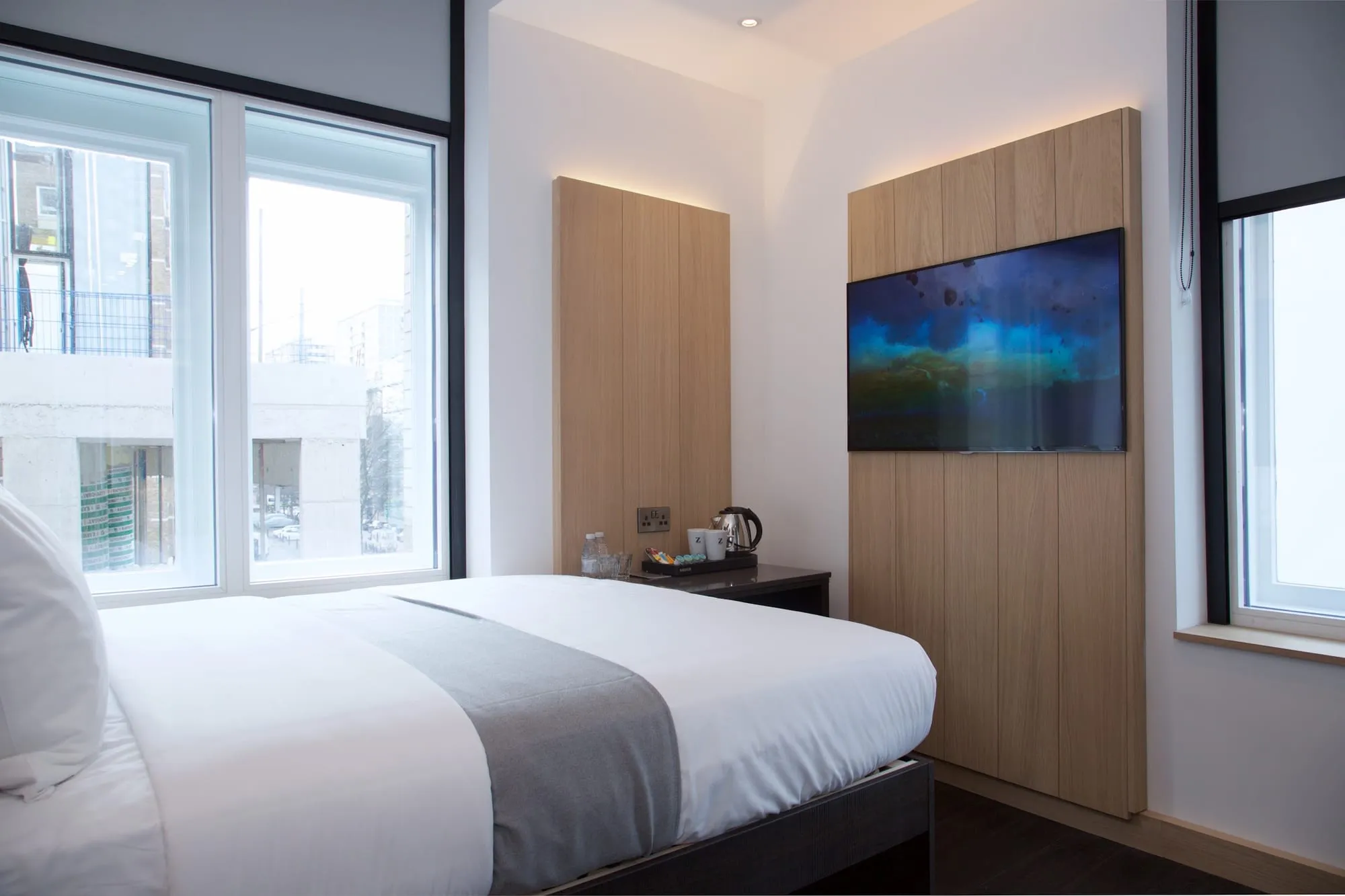 A compact room at the Z Hotel Shoreditch with a wall-mounted TV on a wood panel, and two tall windows looking out over the street
