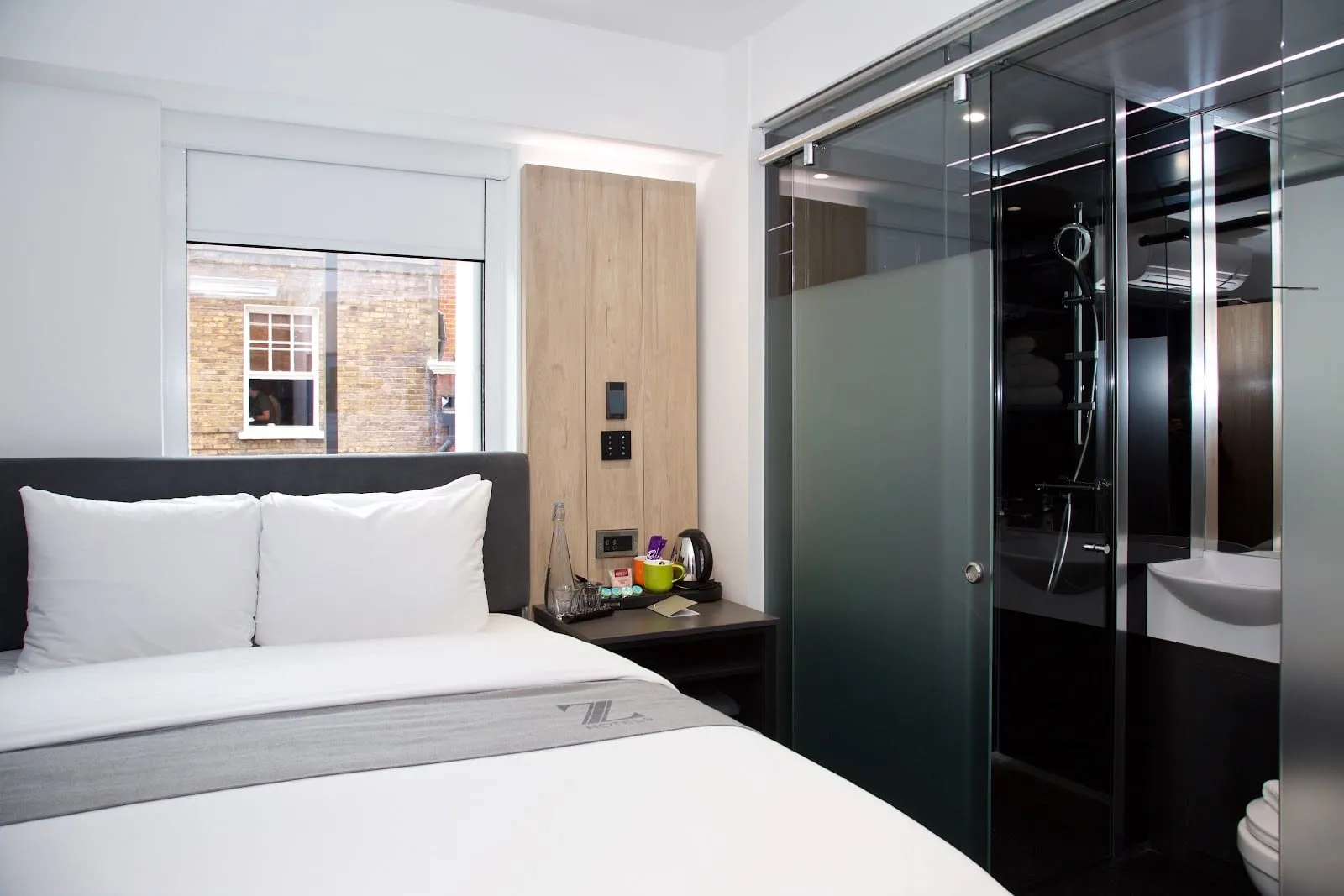 A room at the Z Hotel Tottenham Court Road with a dark upholstered headboard, a wardrobe and desk, and a window looking onto the brick building opposite