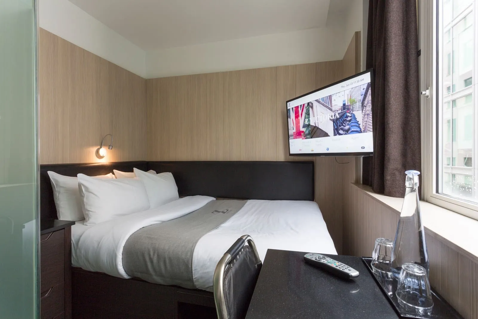 A room at the Z Hotel Victoria with a TV showing the hotel's own welcome screen, and a window looking onto the building next door