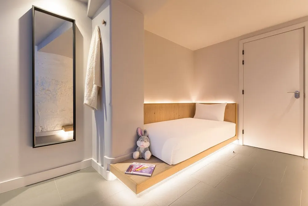 A Zedwell cocoon room with a bed on a lit wooden plinth, a full-length mirror, hooks and a private door