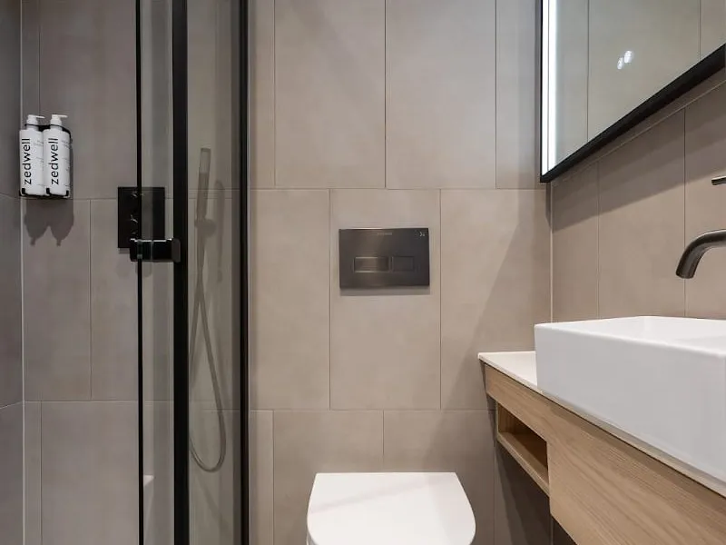 The shower room at Zedwell Knightsbridge in grey tiles, with a glass-doored shower, a wall-hung toilet and a white basin on an oak vanity