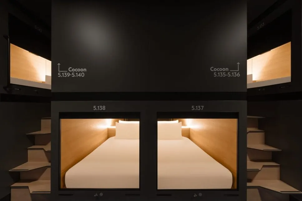 Two numbered Cocoon capsule berths at Zedwell Capsule Piccadilly Circus, each lit from within, with fold-down wooden steps beside them