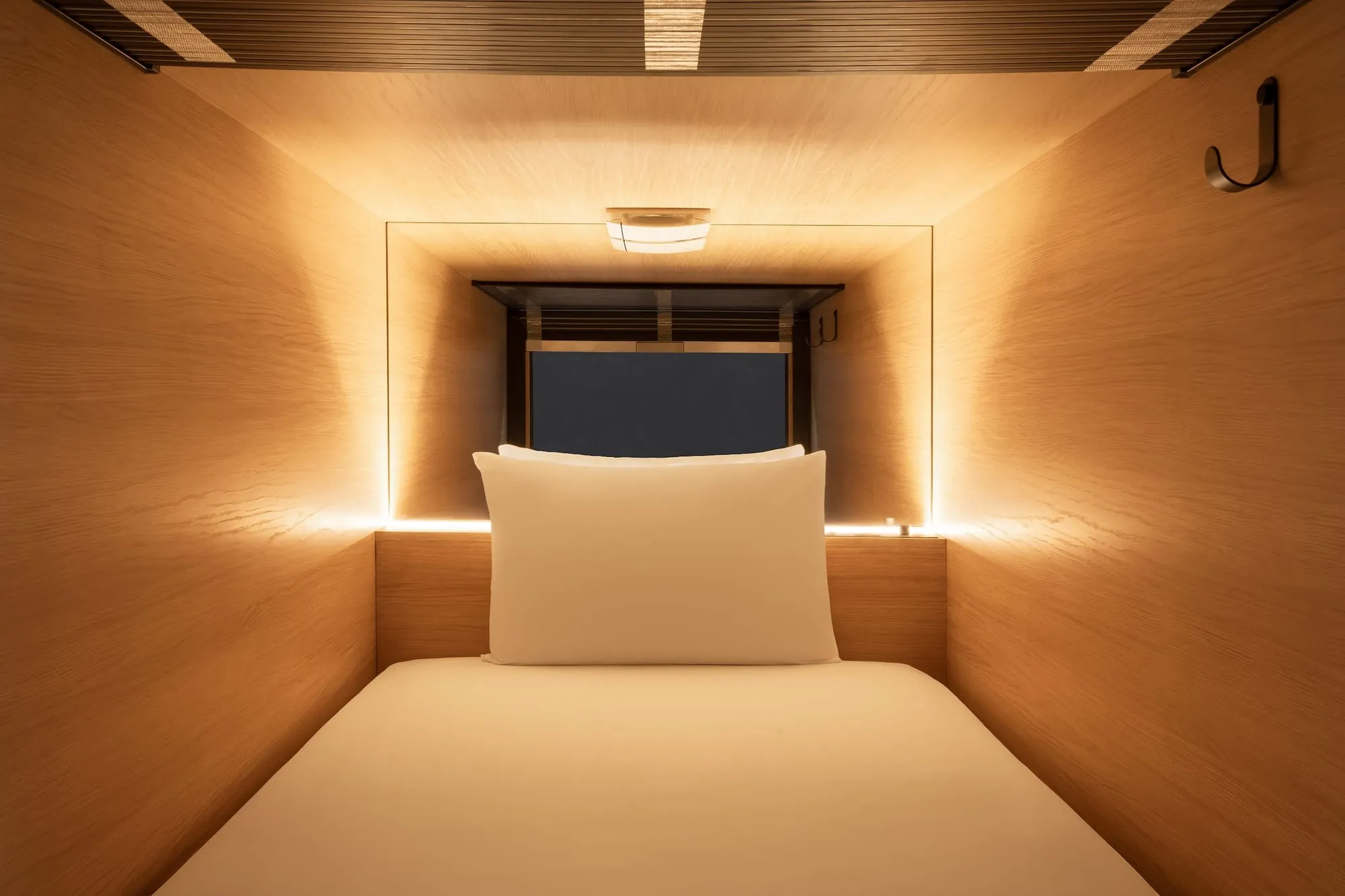 A wood-panelled sleeping capsule at Zedwell's Piccadilly Circus capsule hotel, lit by a warm light strip around the pillow