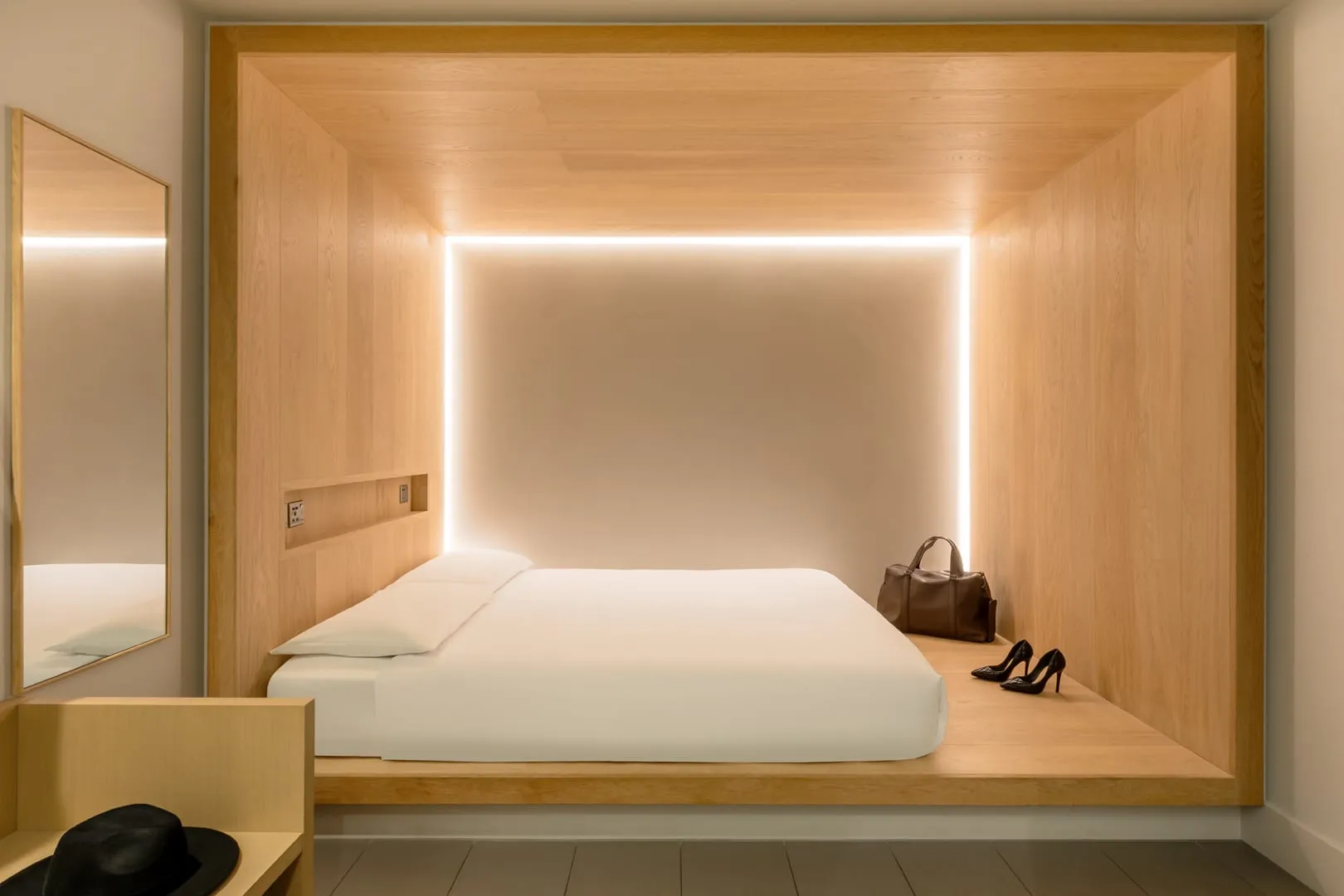 A windowless Zedwell Piccadilly Circus room with a raised platform bed, a wall mirror, and a pair of heels and a handbag on the floor