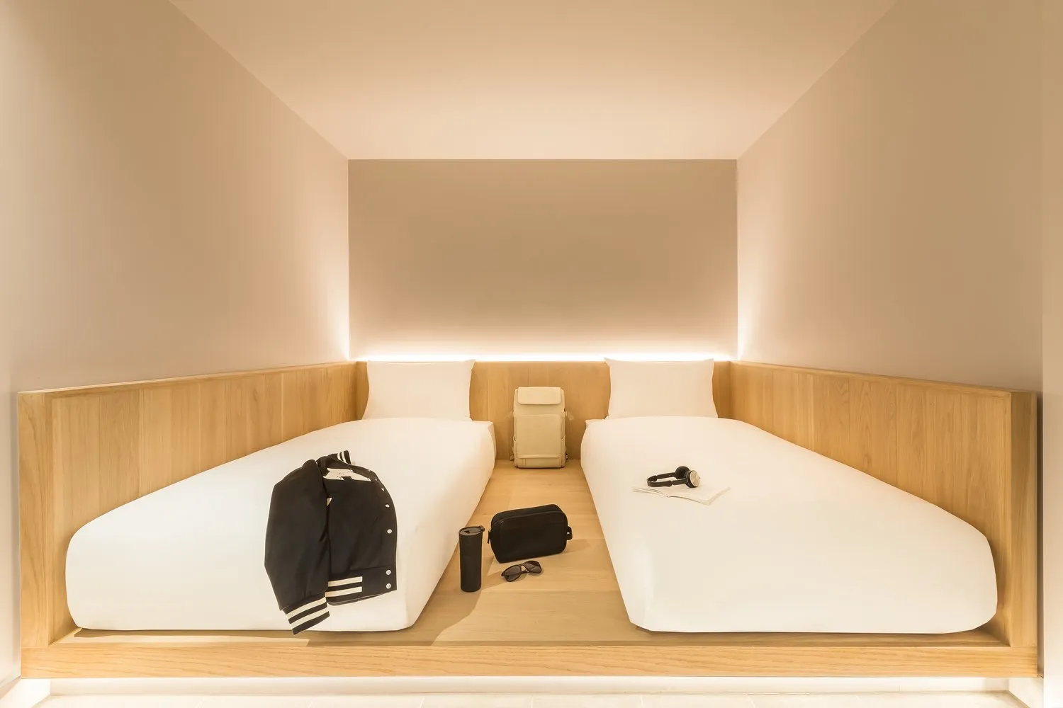 A windowless twin cocoon room at Zedwell Tottenham Court Road with twin beds on illuminated oak plinths and warm recessed lighting