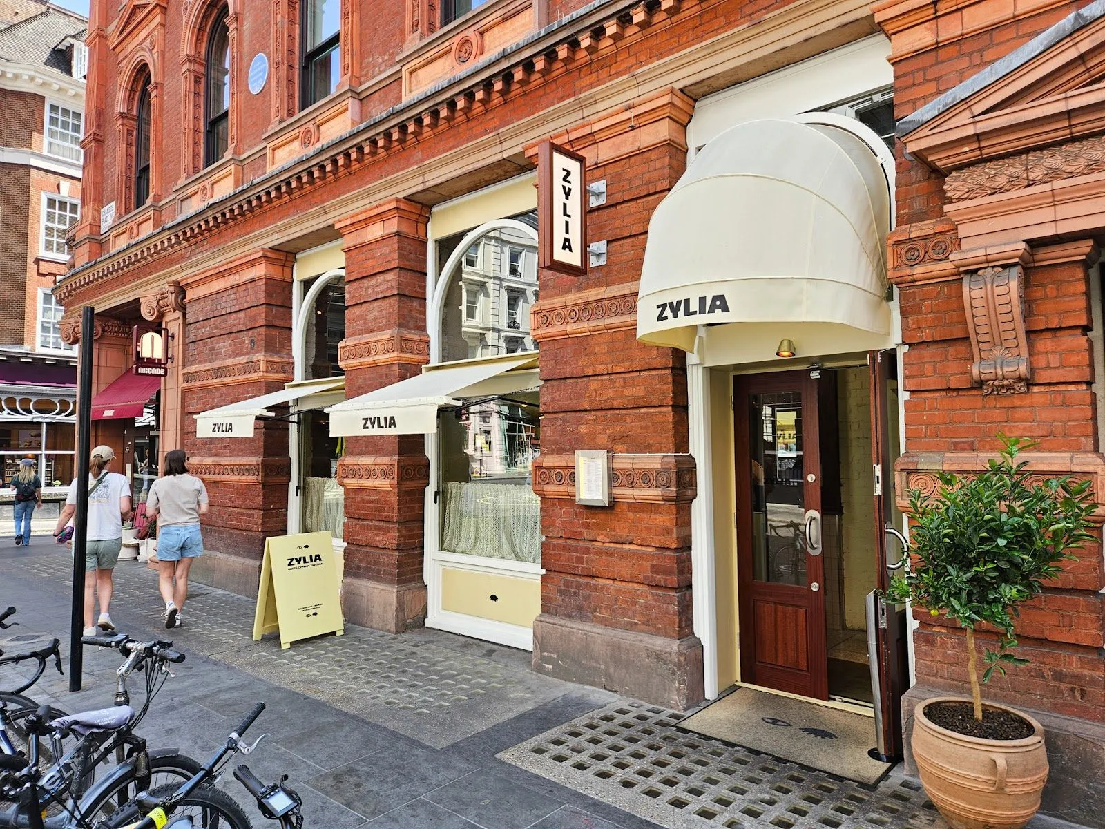 Zylia's entrance on Bedford Street, a red-brick and terracotta building with cream awnings printed ZYLIA, a hanging sign and a potted lemon tree by the door